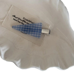 Barrette à cheveux triangulaire à carreaux bleus et blancs sur une coupelle coquillage