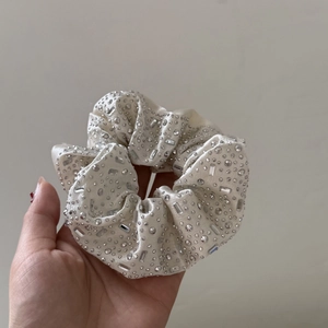 Close-up of cream satin scrunchie with rhinestones held in hand for detail