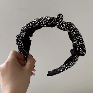 Close-up of black knotted headband with dense silver rhinestones and glossy satin fabric
