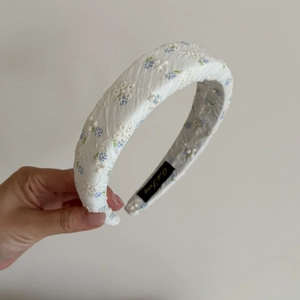 Détail d'un serre-tête blanc épais avec broderie florale bleue et texture de tissu froissé