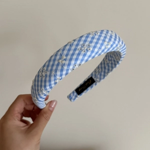 Détail d'un serre-tête à carreaux bleus avec broderies florales blanches et rembourrage