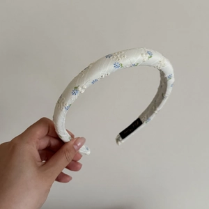 Gros plan sur le serre-tête en tissu beige orné de broderies florales bleues et blanches élégantes