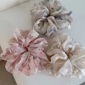 Detail of three mesh hair scrunchies with floral embroidery in blue, pink, and beige colors