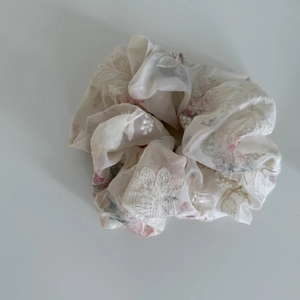 Detail of cream organza scrunchie with delicate pink floral embroidery and soft texture