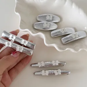 Pinces à cheveux Y2K argentées avec nœuds blancs et strass posées sur un plat en céramique