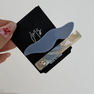 Dettaglio molletta capelli blu e fermaglio in acetato con fiocco dorato su cartoncino