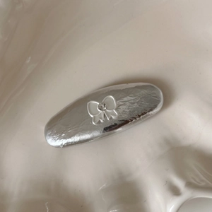 Détail d'une pince à cheveux argentée avec nœud et strass sur une assiette en céramique