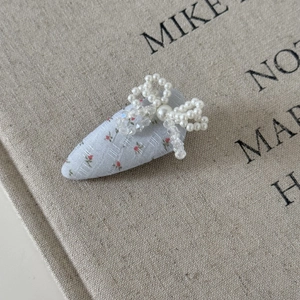 Détail de la pince à cheveux florale avec nœud en perles sur fond en lin beige