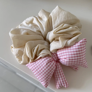 Close-up of beige scrunchie featuring a puffy pink and white plaid checkered bow tie