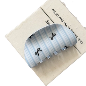 Pinza per capelli a righe blu pastello con motivo a fiocco nero su sfondo crema