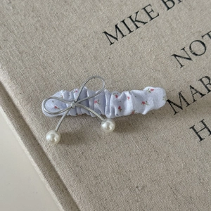Détail d'une pince à cheveux à fleurs avec un nœud argenté et des petites perles blanches
