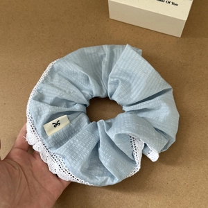 Close-up of blue striped scrunchie with white lace trim and bow logo label detail