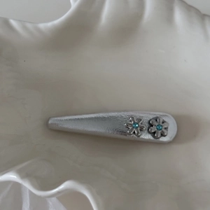 Fermaglio per capelli a fiore argento con strass blu su vassoio bianco