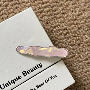 Détail d'une pince à cheveux ondulée en acétate rose irisé avec bordure en métal argenté