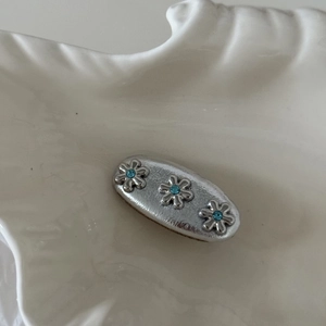 Fermaglio per capelli a fiori argento con strass blu su un vassoio di ceramica