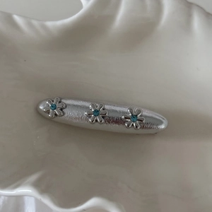 Dettaglio del fermaglio per capelli argento con fiori e strass blu su sfondo bianco