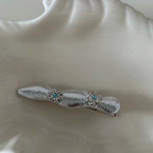 Dettaglio del fermaglio per capelli argento ondulato con piccoli fiori e strass blu