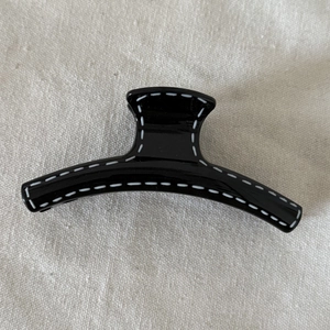 Black resin hair claw clip with white hand-drawn line accents on beige fabric background