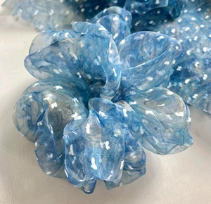 Nahaufnahme von blauem Organza-Scrunchie mit weißen Blumenmustern für Haarstyling