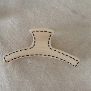 Detail view of cream white hair claw clip with black hand-drawn lines on linen fabric