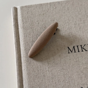 Detail view of a vintage brown plaid fabric hair clip resting on a textured linen book
