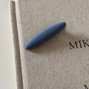 Close-up of deep blue vintage plaid fabric hair clip on a textured linen book cover
