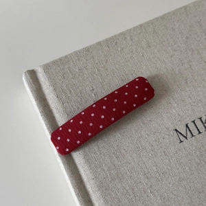 Red fabric hair clip with white polka dots on a minimalist beige linen background