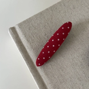 Close-up of red and white polka dot fabric hair clip on a neutral linen background