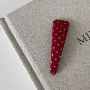 Detail of red fabric hair clip with white polka dots on a textured linen background