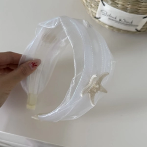 Detail eines weißen Organza-Haarreifens mit Glitzerstruktur und einem cremefarbenen Seestern