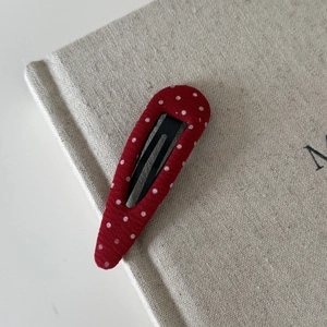Detailed close-up of red and white polka dot fabric hair clip on a textured background