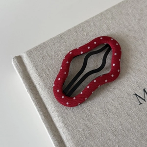 Detailed view of wave-shaped red hair clip with white polka dots on linen background