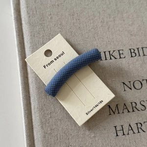 Detail shot of vintage navy blue plaid fabric hair clip on a branded cream-colored card