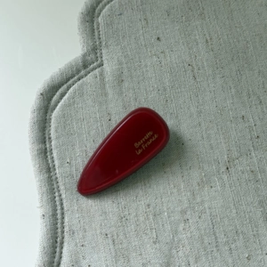 Pink acetate teardrop hair clip with Barrette La France gold lettering on linen