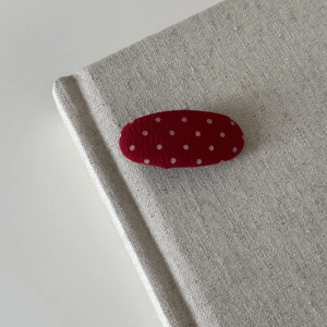 Close-up of red polka dot fabric BB hair clip resting on a vintage book cover