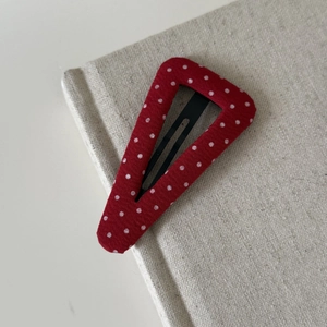 Detail of a red polka dot fabric hair clip placed on a textured beige linen book