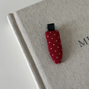 Detail view of red polka dot fabric hair clip on a beige linen book surface