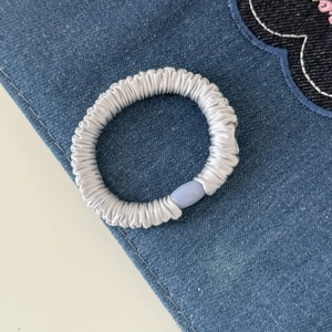Zilvergrijze satijnen haarelastiek met lichtblauwe decoratieve gesp op denim achtergrond