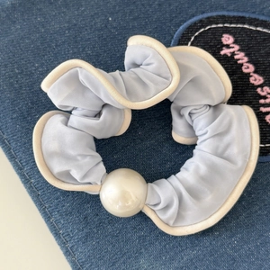 Detail van lichtblauwe scrunchie met witte parel op een blauwe denim achtergrond