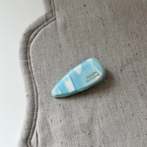 Detailed close-up of blue marble acetate hair clip with gold lettering on a beige mat