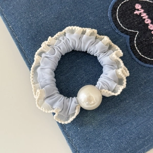 Detail van lichtblauwe parel scrunchie met witte kant op een denim achtergrond