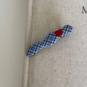 Blue and white checkered wavy hair clip with red 3D heart accent on a beige texture