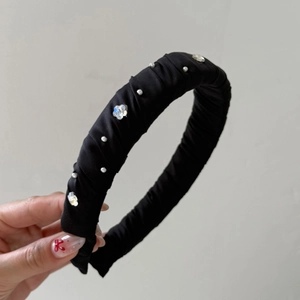 Détail d'un serre-tête en satin plissé noir orné de perles et de strass fleuris