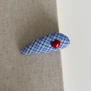 Blue plaid fabric hair clip with a red heart charm on a natural linen background