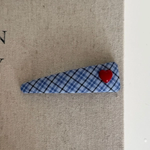 Close-up of blue plaid fabric hair clip with a small red heart accent on linen background