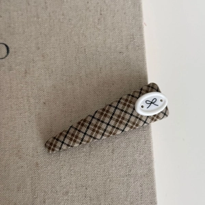 Detailed close-up of a brown plaid fabric triangle hair clip with a small bow accent