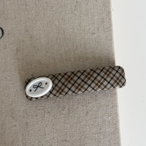 Detailed macro view of the brown plaid fabric hair clip with a white bow button accent