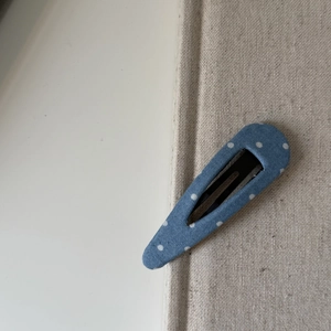 Détail de la pince à cheveux bleue à pois sur un fond texturé minimaliste et chic