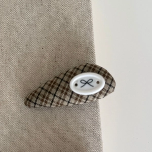 Detail of blue and brown plaid hair clip with bow pattern on a beige fabric background