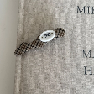Detailed view of the brown plaid fabric texture and oval button on this hair clip